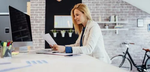 Młoda kobieta siedząca w biurze i sprawdzająca w umowie rachunku swój numer CIF.