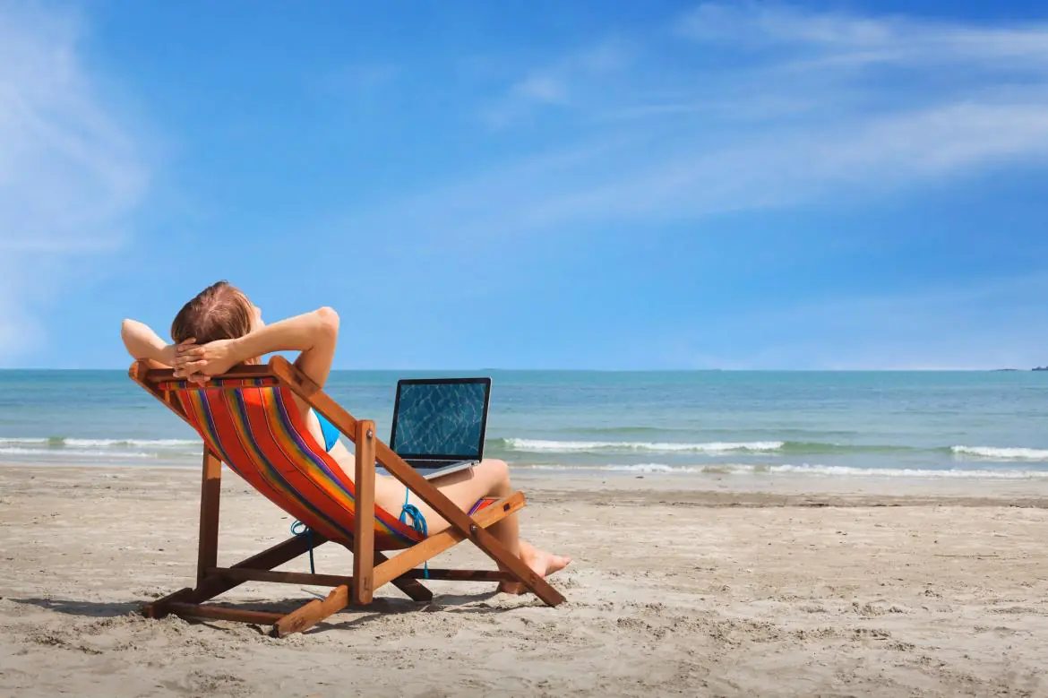 Mężczyzna na plaży, na leżaku z otwartym laptopem na kolanach