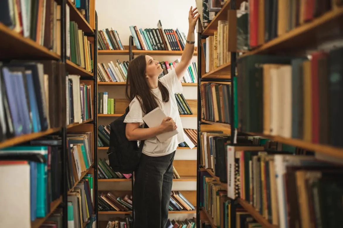 studentka sięga po książkę w bibliotece