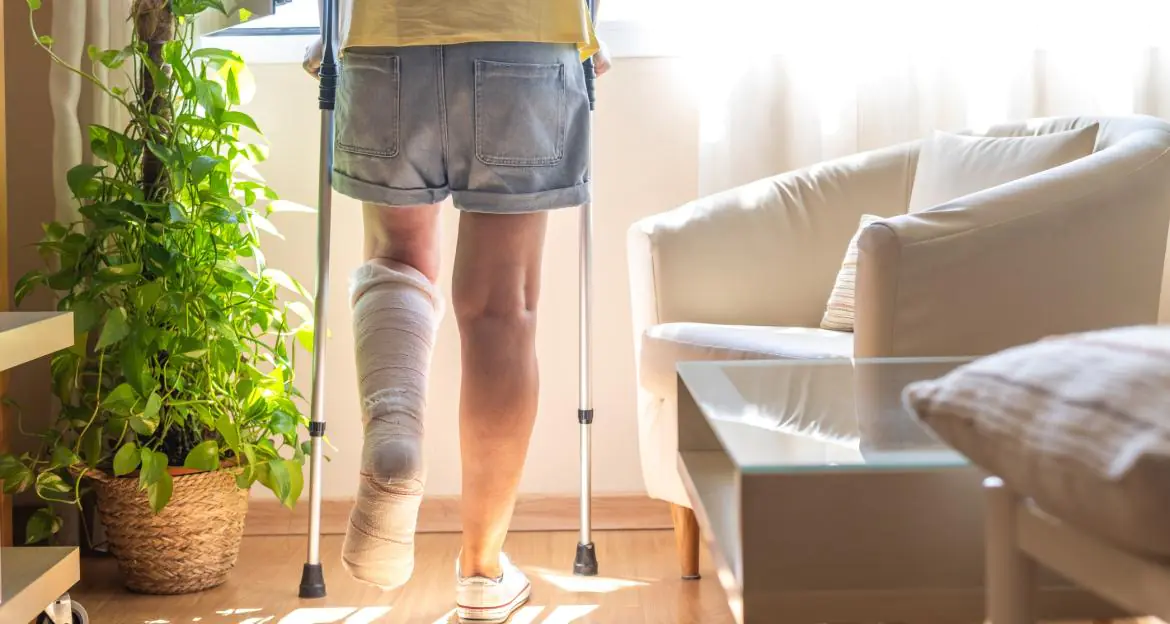Osoba ze złamaną nogą stojąca o kulach w swoim mieszkaniu