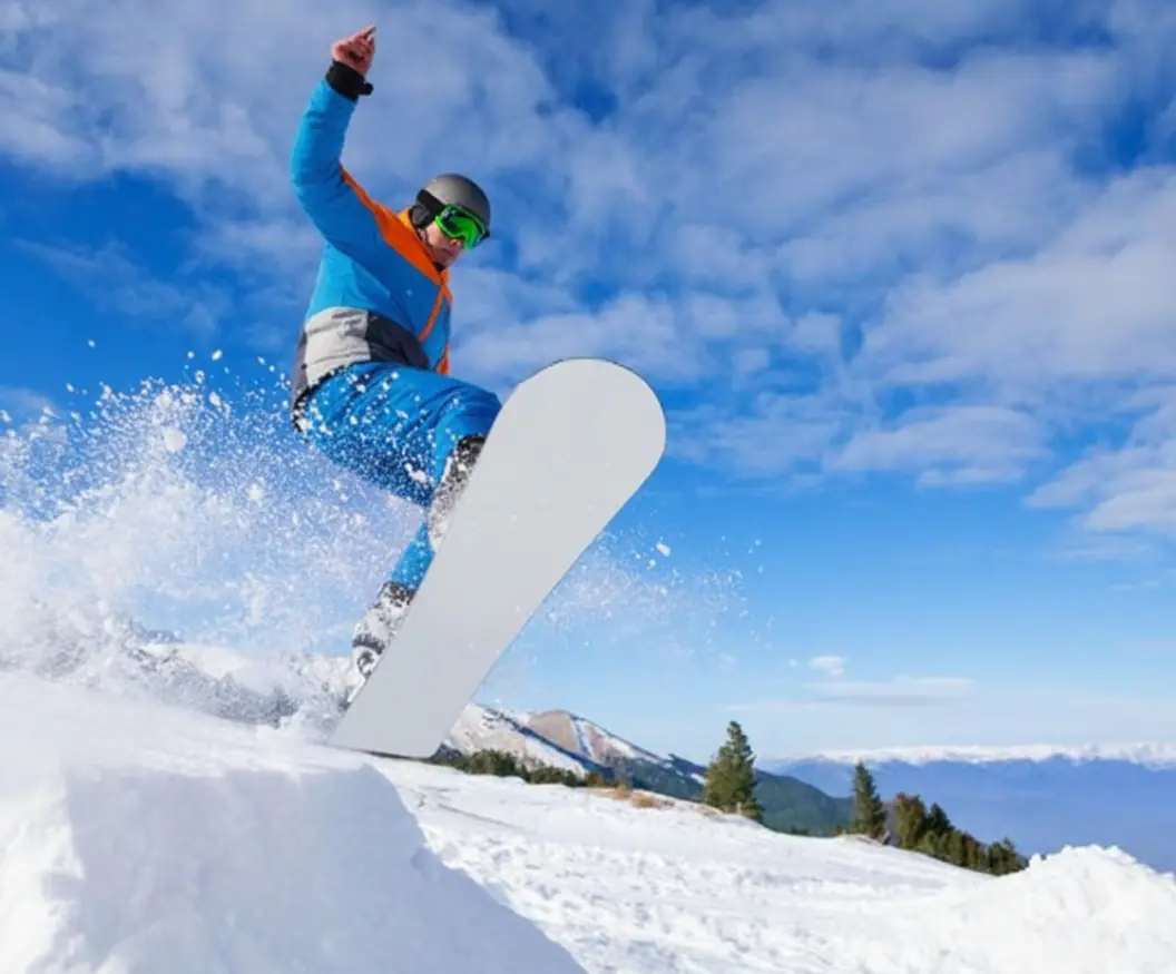 Snowboardzista w niebieskiej kurtce i spodniach wyskakuje z zaśnieżonej muldy