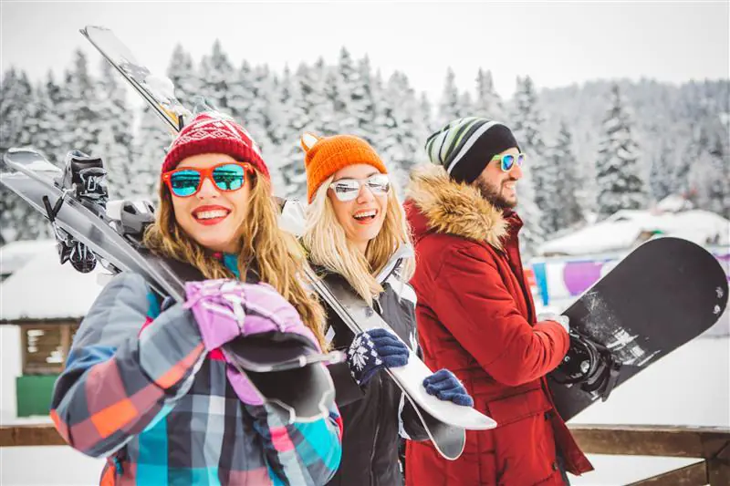 grupa uśmiechniętych znajomych ze sprzętem narciarskim w zimowej scenerii