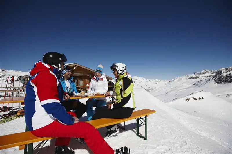 Grupa narciarzy na stoku, siedząca przy stole w słoneczny dzień.