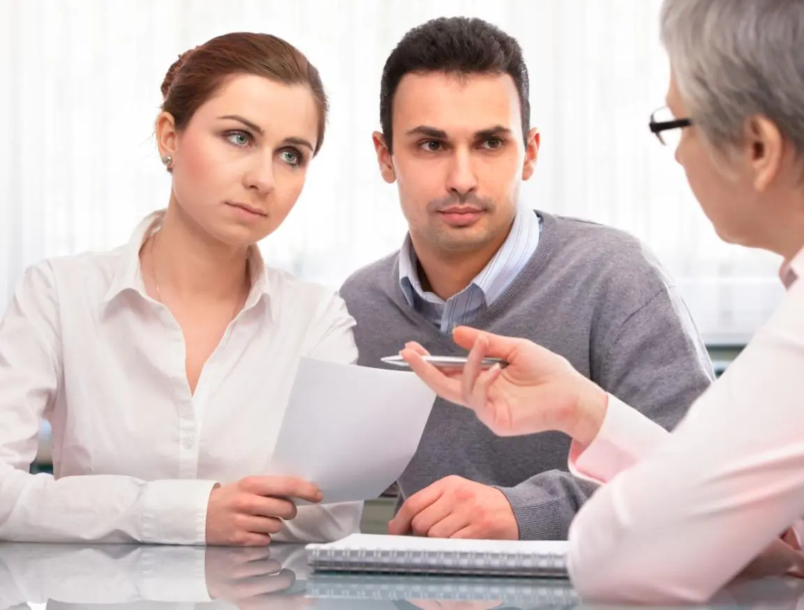 Młoda para podczas rozmowy z doradcą w biurze podróży, analizująca dokumenty i ofertę wycieczki. Opis rozszerzony (na stron