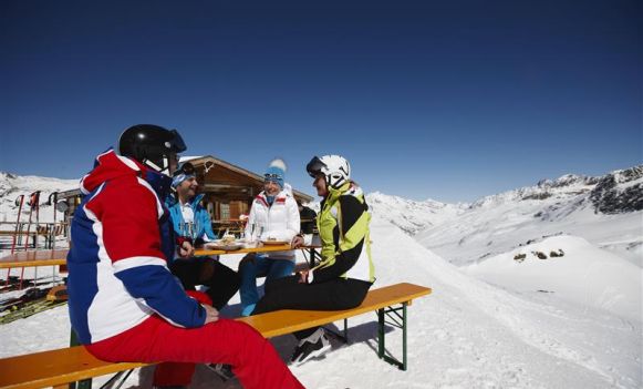 Grupa narciarzy na stoku, siedząca przy stole w słoneczny dzień.