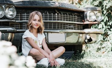Młoda kobieta siedzi obok cadillaca