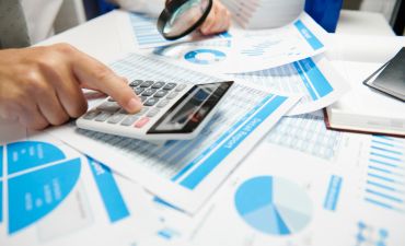 mężczyzna liczący na kalkulatorze wśród wykresów i tabelek