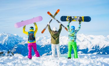 narciarze i snowboardziści na tle zaśnieżonych górskich szczytów