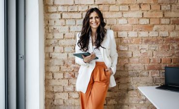 uśmiechnięta kobieta na tle ceglanej ściany trzyma tablet