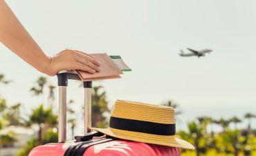 ręka z dokumentami na walizce z kapeluszem, samolot w tle