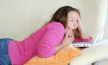 zszokowana kobieta leży na łóżku z laptopem