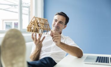 architekt trzyma w ręku drewnianą makietę domu