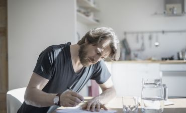 mężczyzna wypełnia dokumenty przy stole w kuchni