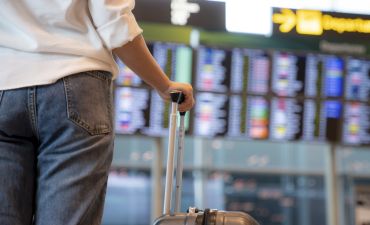 pasażer na lotnisku, z bagażem przed tablicą wylotów