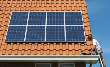 mężczyzna na drabinie montuje panele fotowoltaiczne na dachu