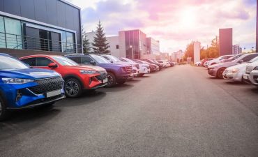 samochody stojące wzdłuż ulicy. W tle chmury i zachodzące słońce. Za samochodami budynki