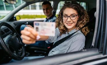 uśmiechnięta kobieta prezentująca do obiektywu swoje prawo jazdy. Obok niej siedzi mężczyzna.