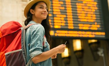 kobieta z plecakiem na lotnisku pod tablicą odlotów