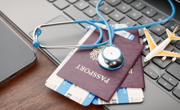 paszport, wizy leżące na klawiaturze laptopa, a na nich stetoskop