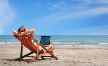 Mężczyzna na plaży, na leżaku z otwartym laptopem na kolanach