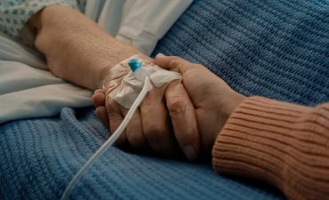 dłoń trzymająca dłoń chorej osoby z wenflonem i kroplówką