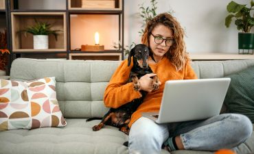 kobieta siedzi na kanapie z psem i czyta coś na laptopie
