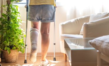 Osoba ze złamaną nogą stojąca o kulach w swoim mieszkaniu