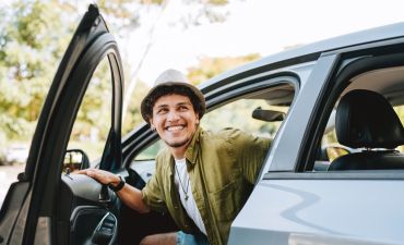 uśmiechnięty młody mężczyzna wysiada z samochodu od strony pasażera