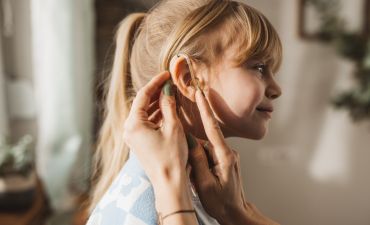 dziewczynka, której ktoś zakłada aparat słuchowy