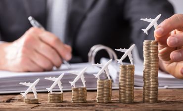 stosy moment, na którymi znajdują się małe samolociki, w tle mężczyzna zapisujący coś w segregatorze