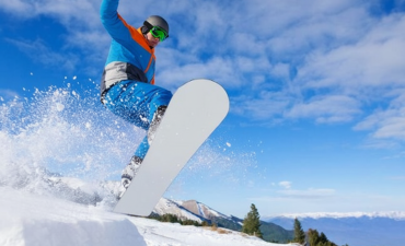 Snowboardzista w niebieskiej kurtce i spodniach wyskakuje z zaśnieżonej muldy