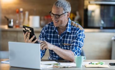 mężczyzna siedzący przy biurku i liczący za pomocą kalkulatora
