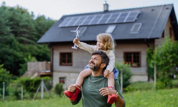 Ojciec z dzieckiem na plecach a w tle dom z fotowoltaiką