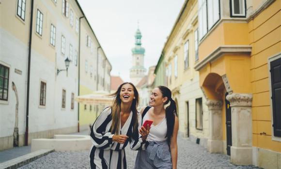 Uśmiechnięte dwie młode kobiety spacerują wąską, brukowaną uliczką Budapesztu