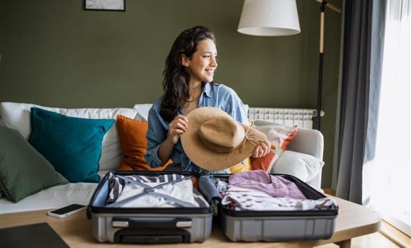 Kobieta pakująca walizkę, trzymająca słomkowy kapelusz w ręku